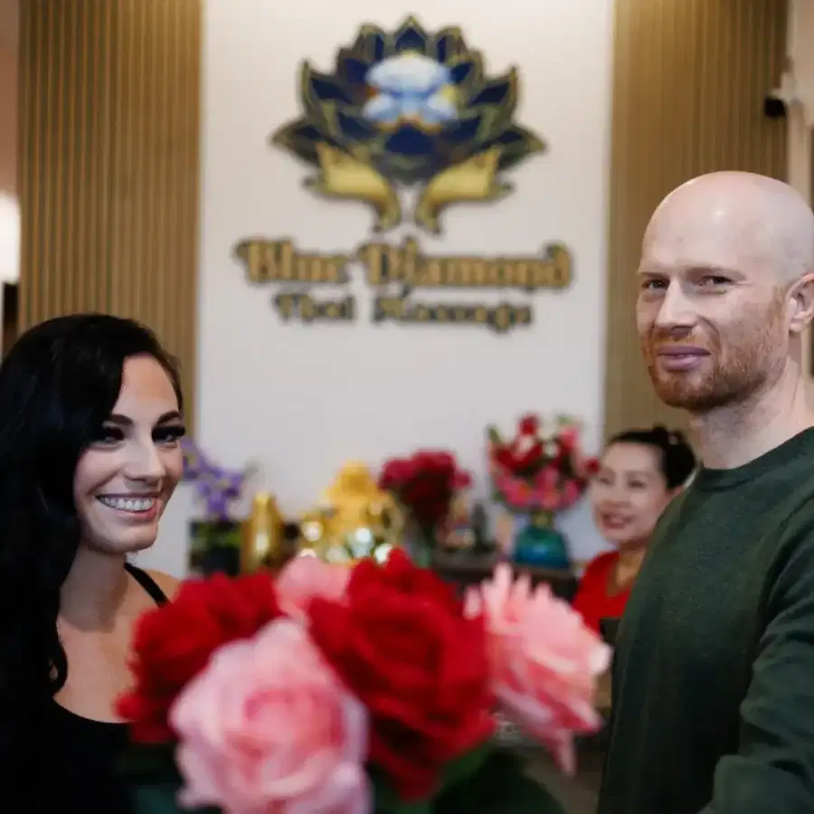 A smiling couple standing in front of the Blue Diamond Thai Massage logo in the reception area